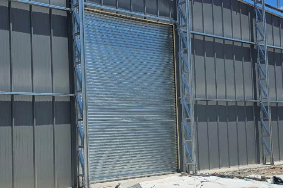 Puerta enrollable metálica cerrada en estructura de andamio, con paneles grises alrededor y suelo de obra.